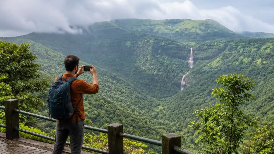 Traveler photographing a green mountain valley and waterfall